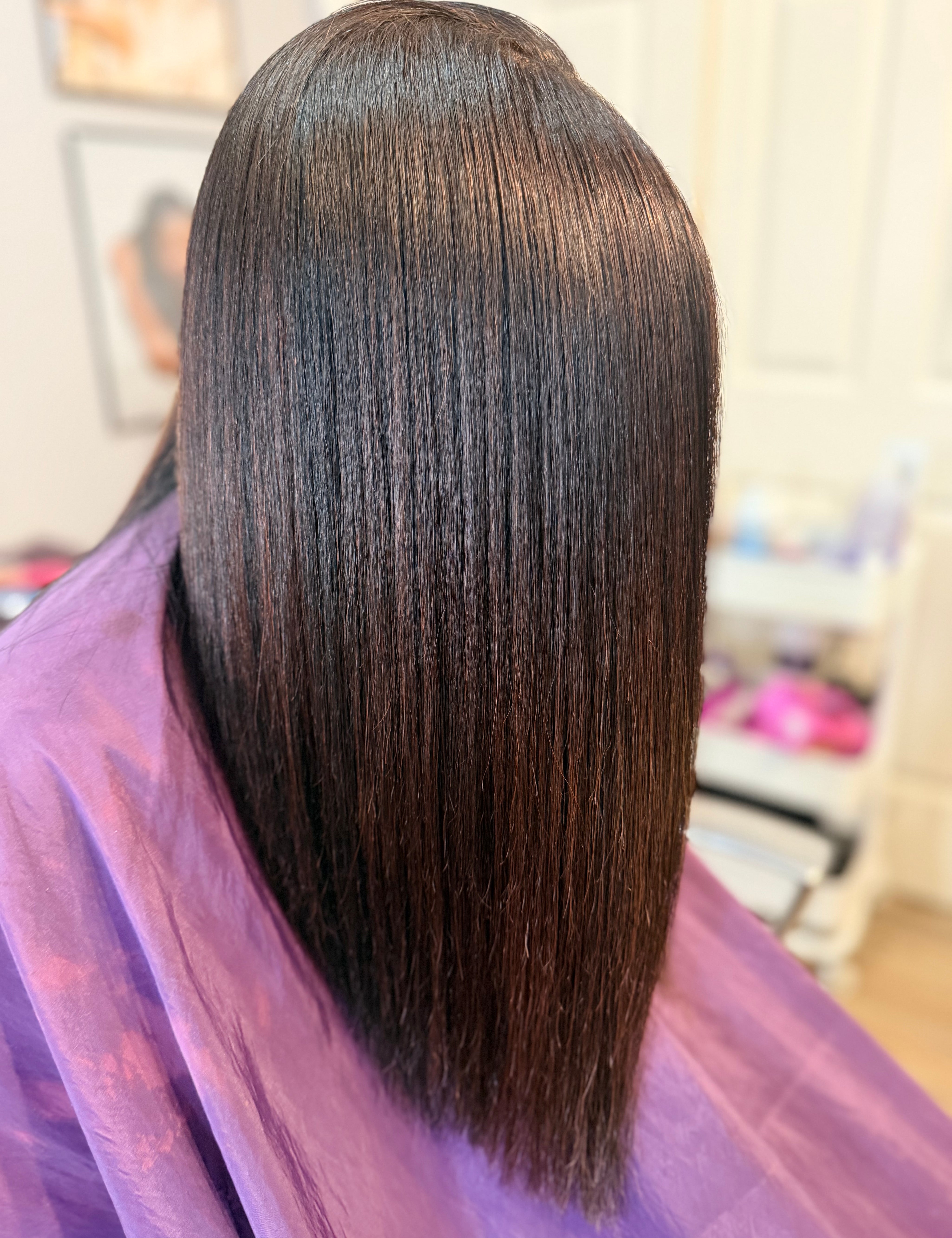 Person with straight, dark hair wearing a purple salon cape. Silk press