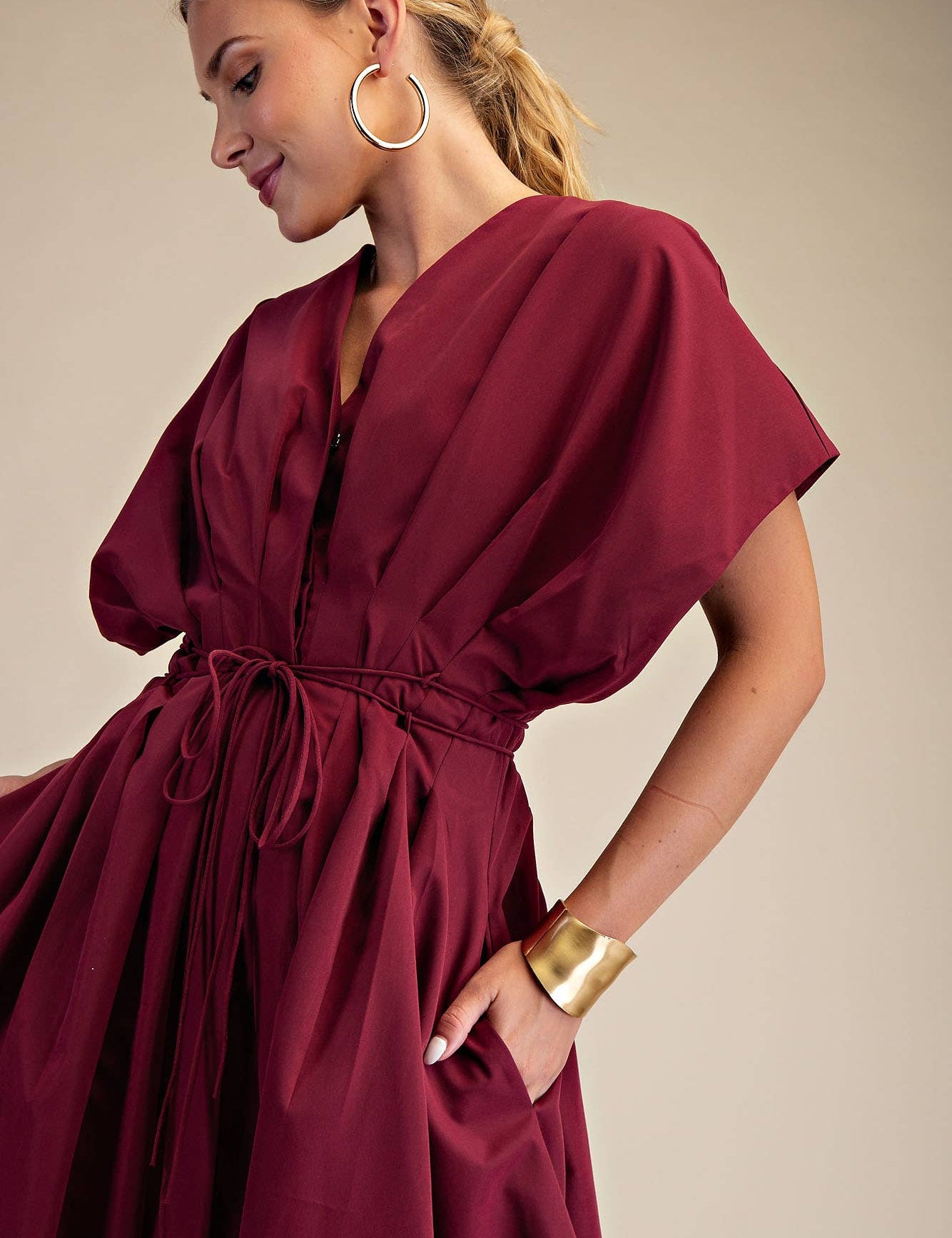Woman wearing a burgundy dress with gold accessories on a beige background